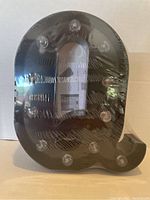 Back of black light-up letter Q showing battery compartment and bulbs for illumination.