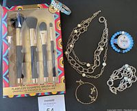 Photo showing cosmetic brush set, jewelry including layered necklace, beaded bracelet, hoop earrings, and two Lokai beaded bracelets