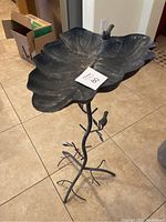 Full view of metal leaf bird bath showing basin, stand, and perched bird figure