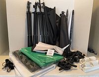 Full kit showing 4 black light stands, 5 black umbrellas, cloth backgrounds in plastic (green, black), piles of white cloth, some clips, cords and white bulb holders.