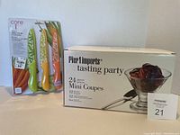 Box of Pier 1 Imports tasting party 24-piece mini coupes set alongside unopened Core Kitchen 3-pack utility knives set in colorful vegetable-themed packaging.