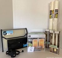 Wide shot showing all items: project paper rolls, two LED candle sets, two portfolio files, and headphones.