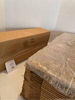 Stack of 25 folded rectangular shipping cardboard boxes bundled together and one box assembled to demonstrate shape and size