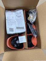 Open box showing sprouted terracotta orange planter modules stacked with black self-watering inserts, instruction manual on top.
