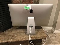 Rear view of the 27-inch Apple LED Cinema Display on a stone surface showing the Apple logo and stand with cable running through the hole.