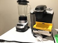 Black & Decker blender and Keurig coffee maker placed side by side on a surface with the water filter cartridges box in front of the coffee maker. Power cords visible.
