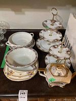Photo showing three Royal Albert tiered cake stands along with several plates and an octagonal teapot with gold accents on a dark surface.