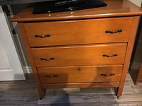 Front view of the three-drawer wooden dresser showing metal handles and scratches on the surface.