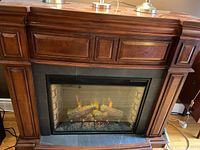 Front view of electric fireplace showing wooden mantel and glowing logs inside the insert.