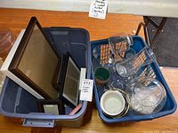 First photo showing baskets with picture frames, glass vases, and ceramic pots on wooden floor.