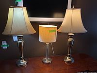Overview of all three lamps together on a table: two taller lamps with urn-shaped bases and bell-shaped shades flank one shorter lamp with cylindrical base and drum shade.