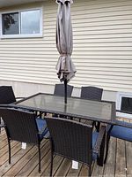 Full ensemble on deck: glass-top wicker table, six chairs, folded umbrella and stand