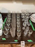 Wide view of assorted stemware on tabletop showing wine glasses, goblets, champagne flutes, textured vintage tumblers, and cocktail glasses.