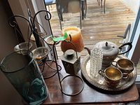 Overall view of the silver plated tea set on tray, the metal lantern, glass vases, candle holders, and a decorative candle arranged together on a wooden surface.