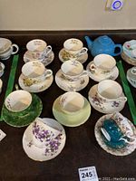 Lot of assorted floral porcelain teacups and saucers with a blue ceramic teapot, arranged on table