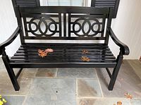 Full view of the black painted outdoor wooden bench with decorative circular pattern on backrest, showing slatted seat and curved armrests.