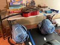 Photo showing the table fully set up with various objects on top and underneath, including board games, a guitar, and dumbbells, confirming the table size and usage context.