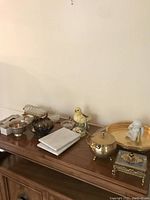 Cut glass coasters on brass holder, porcelain bird figurine, brass sugar bowl, decorative trinket box, brass tray and other assorted items on wooden cabinet