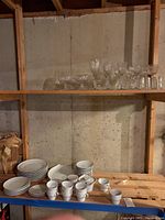 Dishware and glassware displayed on wooden shelves and table, showing plates, cups, and various glassware items.