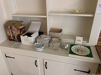 Wide view of all items on white shelf including candlesticks, covered dish, toothpick holders, figurine, and plate.