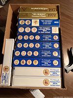 Box with eleven M.J. Hummel annual plate boxes, each labeled with year 1971 to 1979, mostly blue and white boxes with dated text and images of the plate decoration.