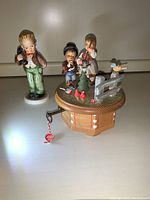 Photo showing the two standalone Hummel figurines and the music box with three figurines on top.