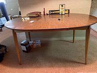 Full view of the mid century modern kitchen table showing the oval wood grain top and tapered legs.