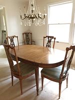 Side angle of oval wooden dining table with four matching chairs under crystal chandelier in dining room.