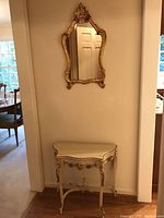 Full view of wall mirror hanging above cream and gold hall table in niche
