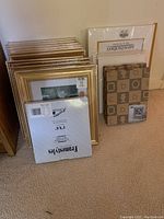 Overview of stacked gold-tone picture frames mostly 8x10 inches with some additional mats and backing boards in packaging.