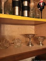 Two weighted sterling silver candy bowls and two cut glass candleholders on a shelf.