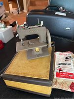 Vintage miniature Singer sewing machine on fabric base with black carrying case and Bondex patch packet beside it.