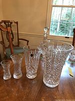 Four Waterford crystal vases displayed on a wooden table, showing a variety of sizes from smallest to largest and intricate cut crystal patterns.