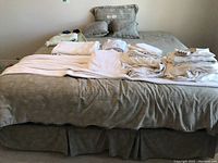 Full view of beige/gray bedspread laid on bed with multiple folded linens and pillows laid on top.