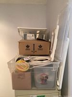 Clear plastic storage bins and cardboard boxes with electrical wires and components inside a shelf space