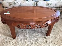 Front view of oval coffee table showing carved floral apron and polished finish