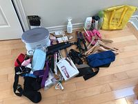 Overview of various personal care items on wooden floor including hot wax bath, curling irons, hand weights, slippers, bags and bottles.