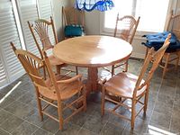 Assembled round oak table top and base shown with surrounding chairs.