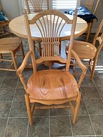 Oak captain chair with armrests in front of round dining table and five matching chairs.
