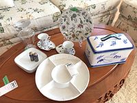 Wide shot of all items on wooden coffee table showing the entire lot contents including divided serving platter, covered dish, salt and pepper shakers, espresso cups with saucers, and decorative floral plate.