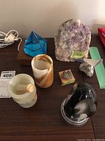 Photo showing the full assortment of the lot on a tabletop including the amethyst geode, marble mortar and pestle, art glass lamp on wooden base, pyrite, and decorative stones.