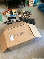 Open box labeled TRAIN with assorted track sections and accessories on floor