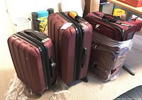 Three burgundy luggage pieces including one Tracker soft roller bag and two Heys hard side roller bags grouped together.