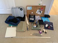 Full overview of the lot showing bulletin board, binders, folders, stapler, keys, locks, rulers, and other office supplies on carpet floor.