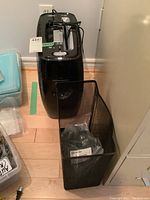 Fellowes P-12C paper shredder with wire shredder basket on floor beside a wall socket and storage bins