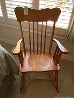 Front view of the solid wood rocking chair showing the seat, spindled backrest, and armrests.