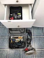 View of partially open drawer containing socket set and case with power tools on the floor