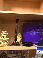 Photo showing two beige stone-like caricature bookends with glasses reading Agatha Christie's 'LES DIX PETITS NÈGRES', two black metal Art Deco candle holders, a small black dish or ashtray, and a purple boxed Transformation game.