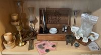 Overview photo showing carved wood box, glass quill holder, brass cross, wooden cups and dishes, shell with sand, metal incense burner, charms in bags, and small ink bottles arranged on a shelf.