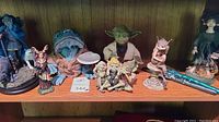 Various fantasy and mythical figurines displayed on a shelf including a Yoda character, a blue wizard, three small whimsical fairies, and a goblin figure